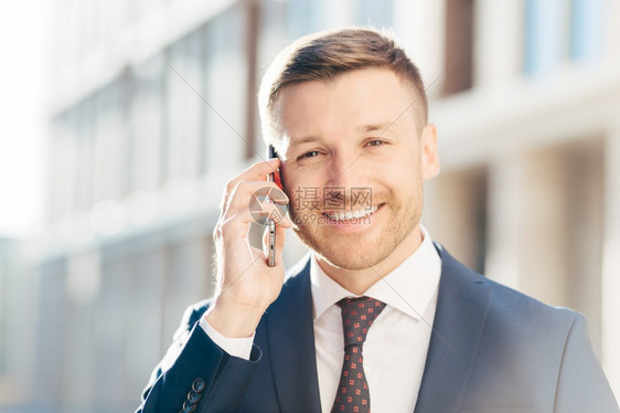 令人愉快的欧洲商肖像穿着优雅的西装讲智能电话与商业伙伴打交道决定会议时间有正面的表情图片