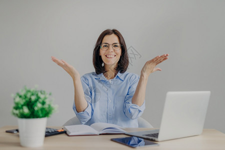 快乐的女子在工作上取得成功高果快乐地举手坐在工作场所用笔记本电脑日计算器隔离在灰色背景上图片