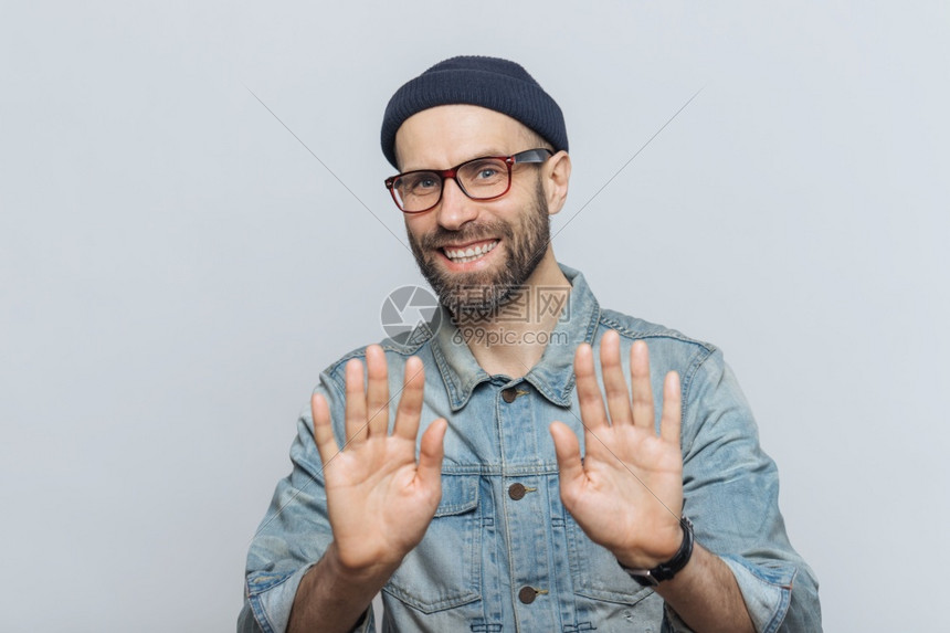带着迷人的外表快乐戴着时装黑帽子牛仔夹克和眼镜的年轻男在室内摆姿势高清图片下载 正版图片 摄图网