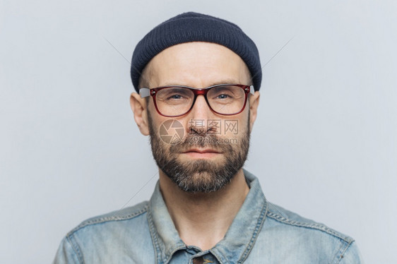 有智慧自信胡子和的时尚男照片认真看待相机面对灰色工作室背景佩戴眼镜和帽子面部表情概念图片