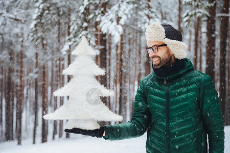 中年微笑的男在人造白小fir树上笑的表情庆祝新年节日在雪天下森林中度过清晨新鲜空气图片