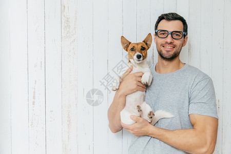 快乐的未分形男穿便衣抱着小狗一起走路站在用空白的复写间站在白木墙上图片