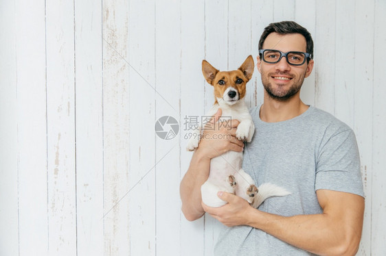 快乐的未分形男穿便衣抱着小狗一起走路站在用空白的复写间站在白木墙上图片