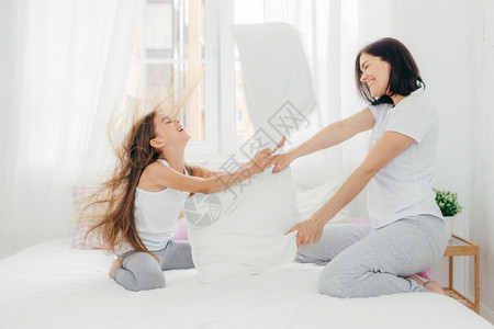 具有积极微笑的吸引力女母亲与儿自由相处与女儿玩枕头搏斗与室内卧作对周末享有休闲时间图片