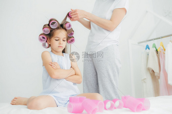 阴郁的女婴把胳膊折起来头部有卷的发她母亲站在附近做头发风卷尾准备生日派对照顾美貌和外童年概念图片