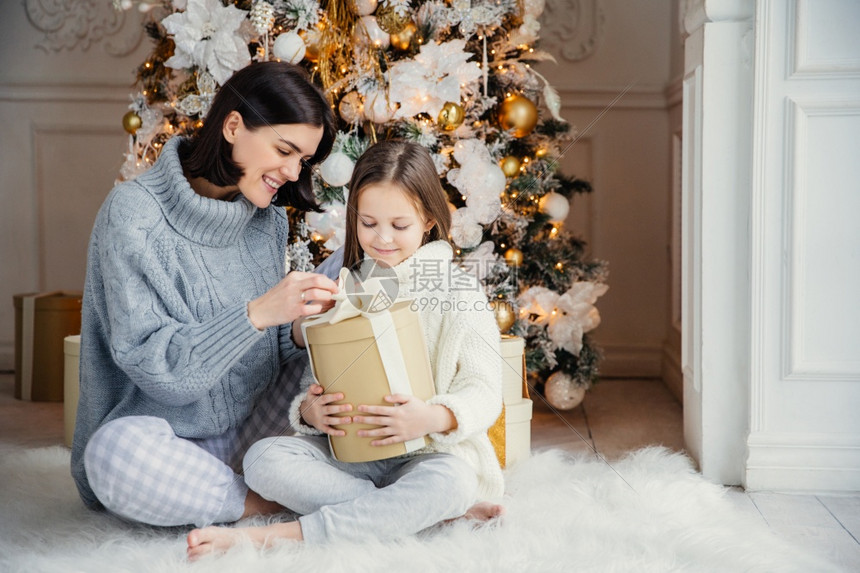 美丽的女孩和母亲肖像一起坐在温暖的地毯上拿着这个盒子享受盛装的新年树图片