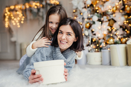 圣诞节图片这是给你的快乐小孩拥抱着她亲切的母带着包的礼物站在装饰背景与园林和新年树家庭气氛背景