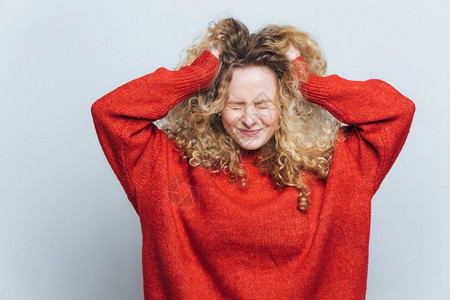 沮丧的金发女人哭出头后悔做错事表达负面情绪穿松散的红毛衣孤立在白色工作室背景图片