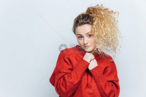 穿着红色毛衣以不自信的镜头表情看用空白的复写间向墙上竖立图片