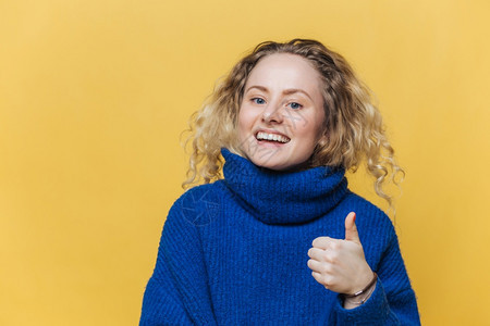 女模范满足于某事举起拇指高兴的表达穿蓝色毛衣配制黄工作室背景图片