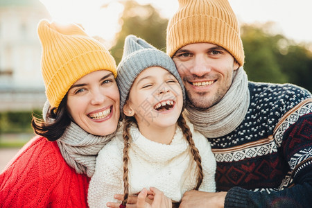 笑的幸福女人和男的横向肖像与女儿玩得开心穿戴编织的帽子温暖毛衣和围巾图片