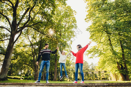 友善的亲家庭肖像合在一起玩乐户外闲时间反对公园绿树试图将小孩摇在手里图片