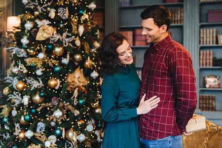 漂亮的妻子站在丈夫身边为她准备了新年礼物良好的关系概念男女反对神圣的诞树冬季假期背景图片