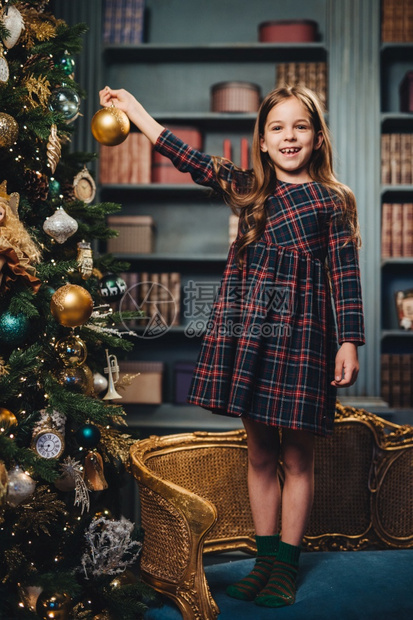美丽的小女孩站在扶手椅上拿着玻璃球装饰新年树乐于这样做可爱的小孩忙着装饰圣诞树图片