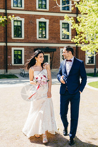 穿着白色婚纱的美丽年轻新娘拿着花束与她未来的丈夫交谈一起散步去登记处图片