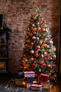 圣诞树上装饰着明亮的圣诞树旁边有一堆礼物盒站在砖墙前圣诞树和礼物图片