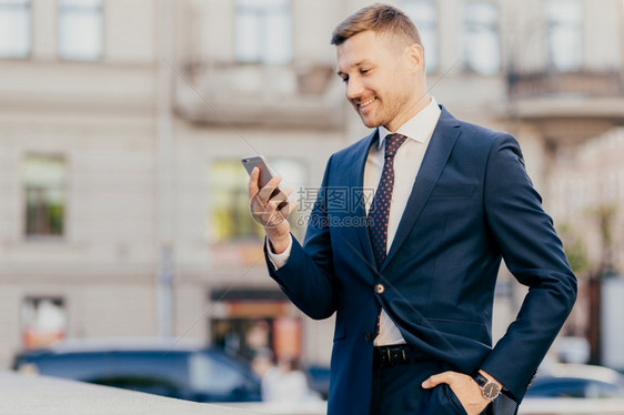 快乐的商人横向拍摄保持手口袋穿正式的西装和手表重新在智能手机上发布通知现高度的财政平衡图片
