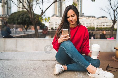 年轻美女坐在户外时使用手机的肖像图片