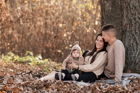 年轻父母亲和女婴在阳光明媚的日子里在秋天公园的毛毯上放松图片