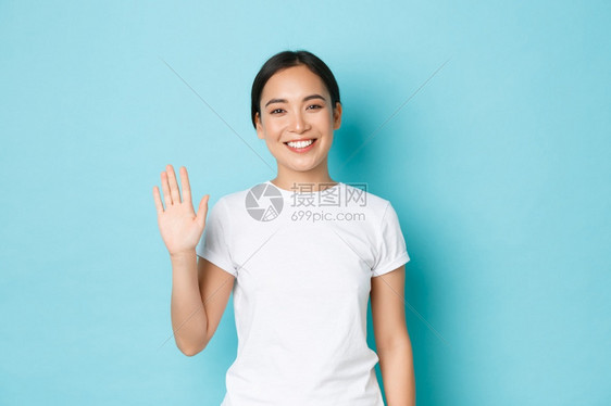 站在蓝背景欢迎某人身穿白色t恤的友好快乐亚洲女孩肖像向大家问好人们微笑和挥手图片