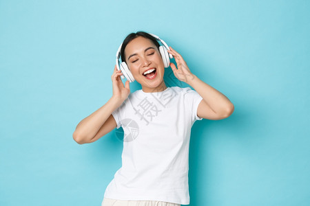 购物金钱和融概念欢快的亚洲女孩穿白色散装t恤唱卡拉ok播放音乐应用程序听无线耳机音乐并享受完美的声音购物播放音乐应用听无线耳机音背景图片