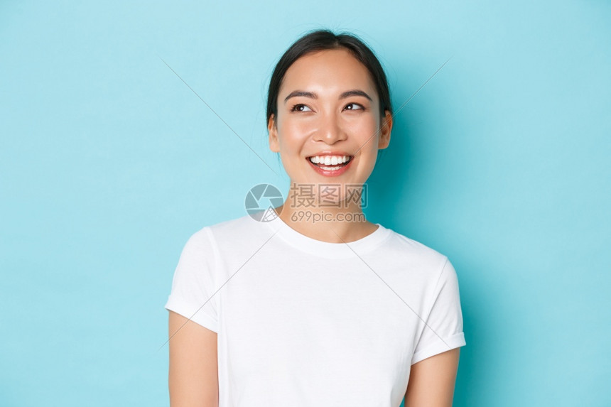 身穿白色t恤衫的梦幻般亚洲女孩穿着白色t恤看充满希望和快乐的左上角大笑和在浅蓝背景上站着快乐的笑容复制空间身穿白色t恤的梦幻般亚图片