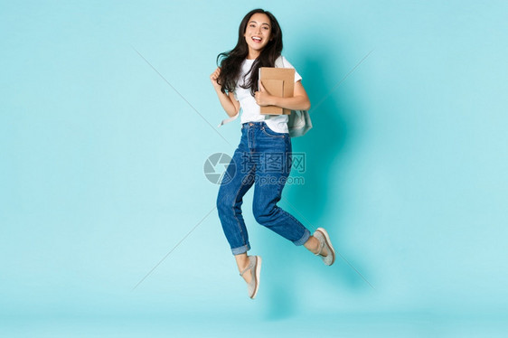 时装回到学校和生活方式概念快乐的年轻亚洲女孩快乐的韩国学生快乐的年轻亚洲女孩带着背包和笔记本在浅蓝背景上跳起来时装回到学校和生活图片