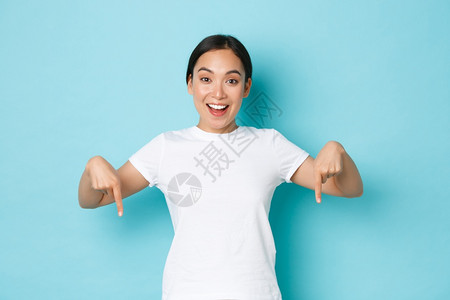 身穿白色t恤的快乐年轻女身穿白色t恤手指向下微笑着兴奋的看自己图片