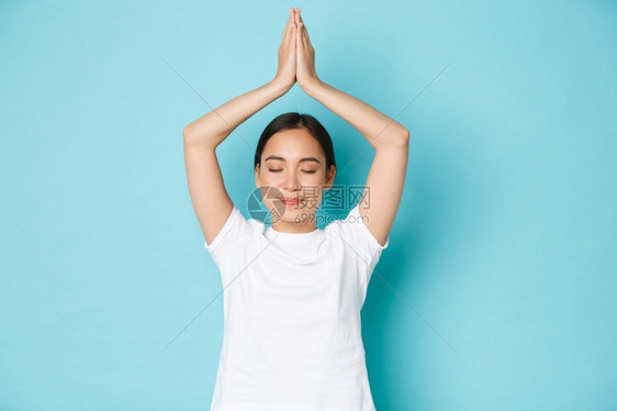 关注其心理健康练习瑜伽或冥想闭眼和举起手顶头部穿戴蓝色背景关注其心理健康闭眼和举起手顶头部蓝背景图片