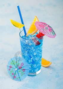 蓝色环礁湖夏季鸡尾酒放在高球玻璃中有甜鸡尾酒樱桃和橙色切片蓝桌底有伞图片