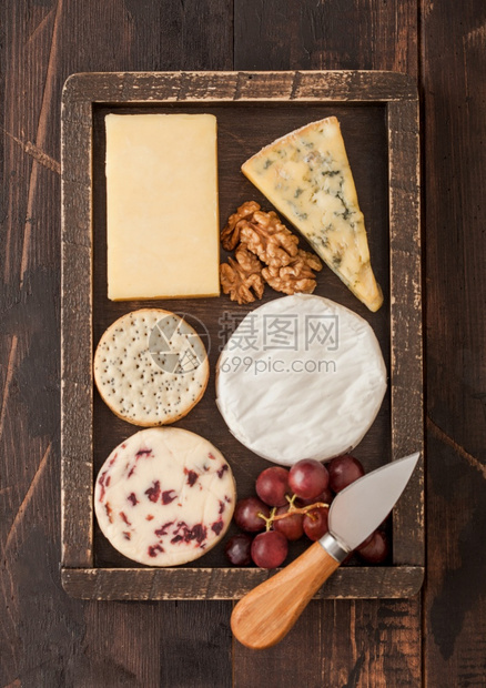 在木制盒子中选择各种奶酪木制桌底有葡萄和坚果图片