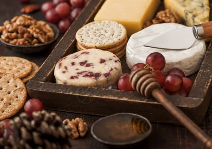 在木本底的古董盒葡萄中选择各种奶酪蓝宝石红色李斯特白奶酪和加饼干蜂蜜的坚果图片
