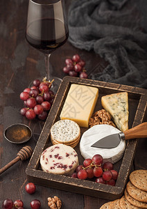 一杯红葡萄酒在木箱中挑选各种奶酪和木底葡萄蓝色的stilon红色的李斯特面包奶酪和一碗加蜂蜜的坚果图片