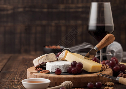 玻璃红葡萄酒在板上挑选各种奶酪和木制桌底的葡萄蓝色stilon红色的李斯特面包奶酪和带蜂蜜的刀子图片