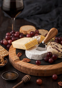 玻璃红葡萄酒在板上挑选各种奶酪和木制桌底的葡萄蓝色stilon红色的李斯特面包奶酪和带蜂蜜的刀子图片