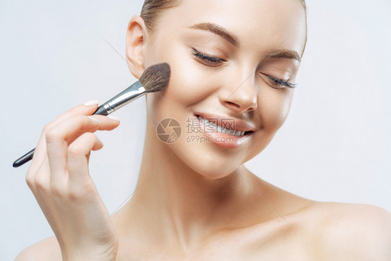 具有健康软皮使用化妆粉刷在脸上打地基有纯净的外衣天然化妆品室内高分辨率的欧洲女阳柔软皮肤室内站立图片