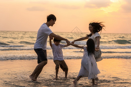 父亲和母亲和孩子在日落时一起在海上玩耍图片