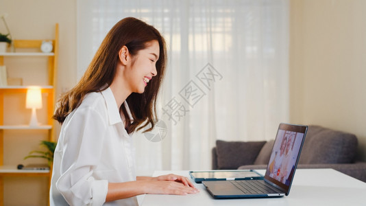 年轻女商人使用笔记本电脑视频话在客厅家工作时与庭父亲和母交谈图片