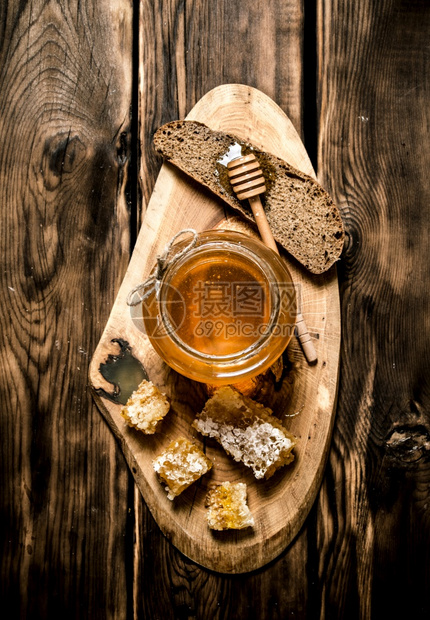 装有蜂蜜和一块面包的玻璃罐放在木制背景上装有蜂蜜和一块面包的玻璃罐图片