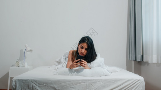 醒来后躺在床上玩手机的女孩图片