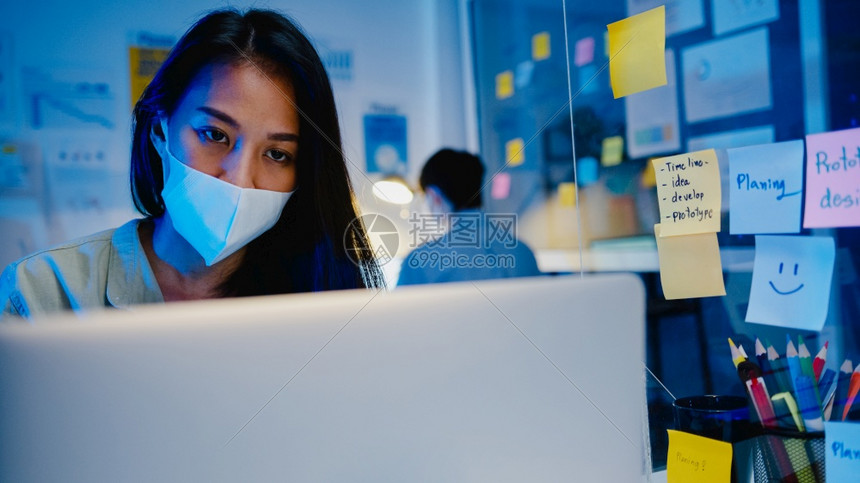 身戴医疗面罩的快乐女商人身着医疗面罩在预防的新正常情况下使用笔记本电脑图片