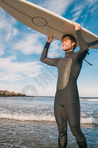海滩上年轻冲浪手的肖像举起他冲浪板穿着黑色冲浪西装运动和水上的概念图片