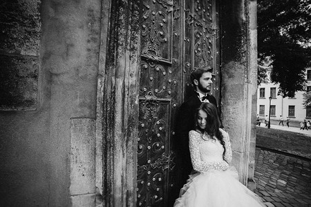 黑白照片结婚夫妇在古老的绿门附近拥抱古城背景的石墙穿着蕾丝裙的长发新娘穿西装的郎和领结婚夫妇在古老的绿门附近拥抱穿着长发新娘西装图片