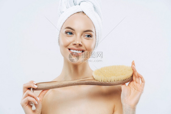 年轻女有健康的新鲜皮肤使用身体刷子轻地微笑头上戴浴巾无衣与白背景隔绝图片
