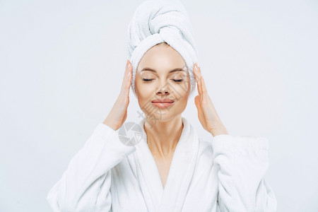 美丽的水疗女闭着眼睛站手放在头部的毛巾上穿着白浴袍皮肤健康天然化妆图片