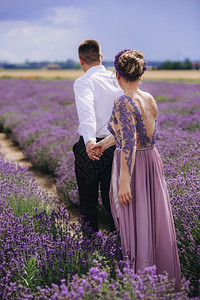 爱的年轻夫妇在夏季阴云的白天在熏衣草地上手牵散步穿着豪华紫色裙子和发型的年轻夫妇在夏季阴云的白天在熏衣草地上手牵散步穿着豪华紫色图片