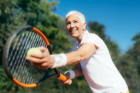 以网球为娱乐活动而打网球的笑着老年妇女图片