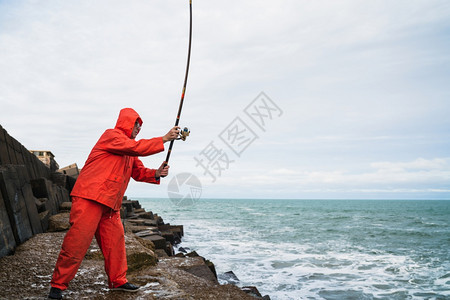 一个老人在海边岩石上钓鱼的肖像概念图片
