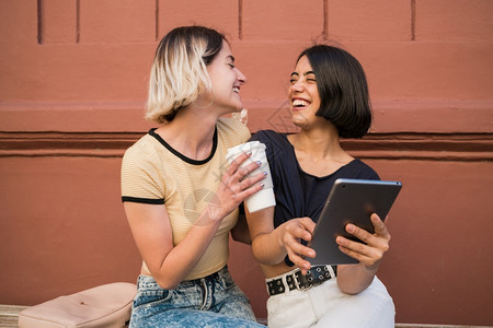 可爱的女夫妇在街上共度时光,并用数字平板电脑在户外自拍。 lgbt概念。图片