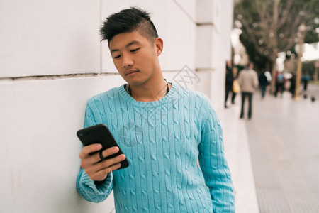 年轻亚洲人使用手机在街上户外站立的肖像图片